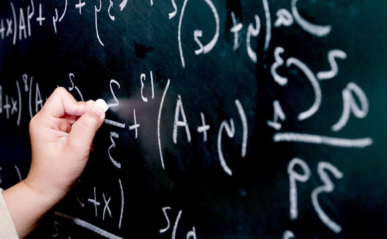 Hand with chalk writing mathematic equations on a chalk board